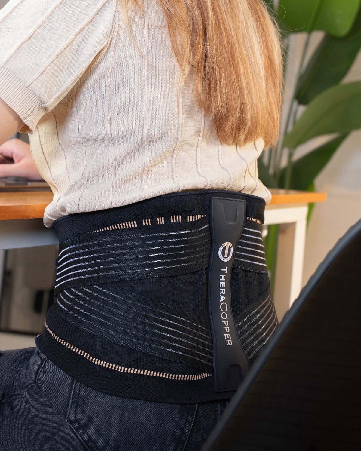 Woman seated at a desk wearing the TheraCopper lower back brace