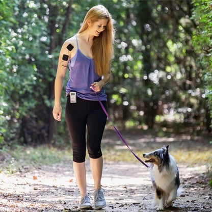 Woman walking a dog outdoors with TENS pads on her upper arm